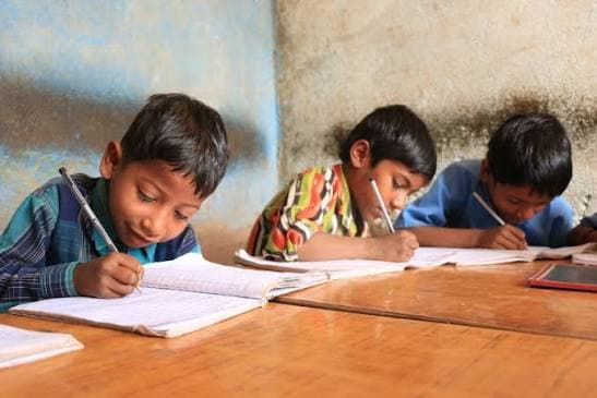 Three boys writing in their notebooks at a classroom desk